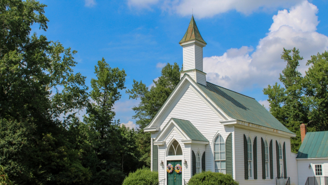 Attēlā maza, balta baznīca starp kokiem