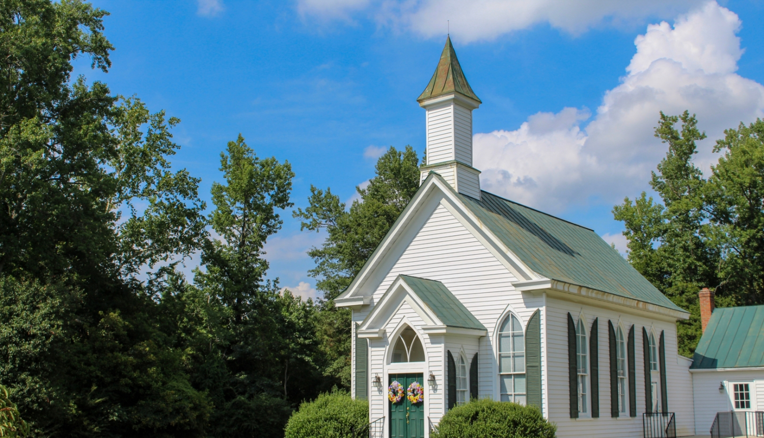 Attēlā maza, balta baznīca starp kokiem